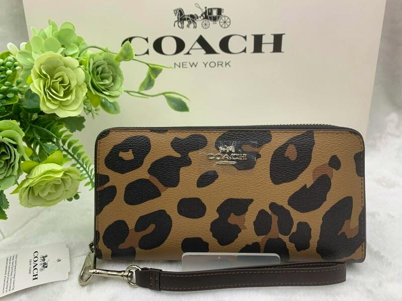 Front view of the COACH long leopard-print zip-around wallet with visible metal COACH logo and detachable wrist strap.