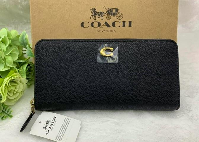Black COACH long zip-around wallet displayed closed in front of a COACH box with its tag visible.