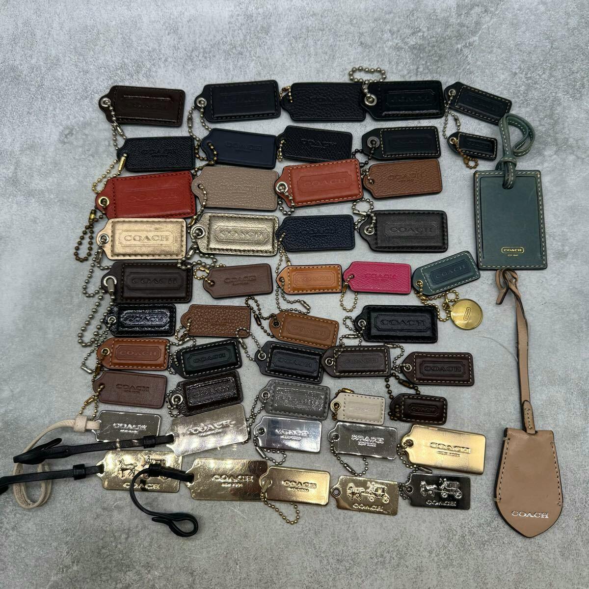 Many COACH leather and metal keychain and bag charms arranged on a gray surface.