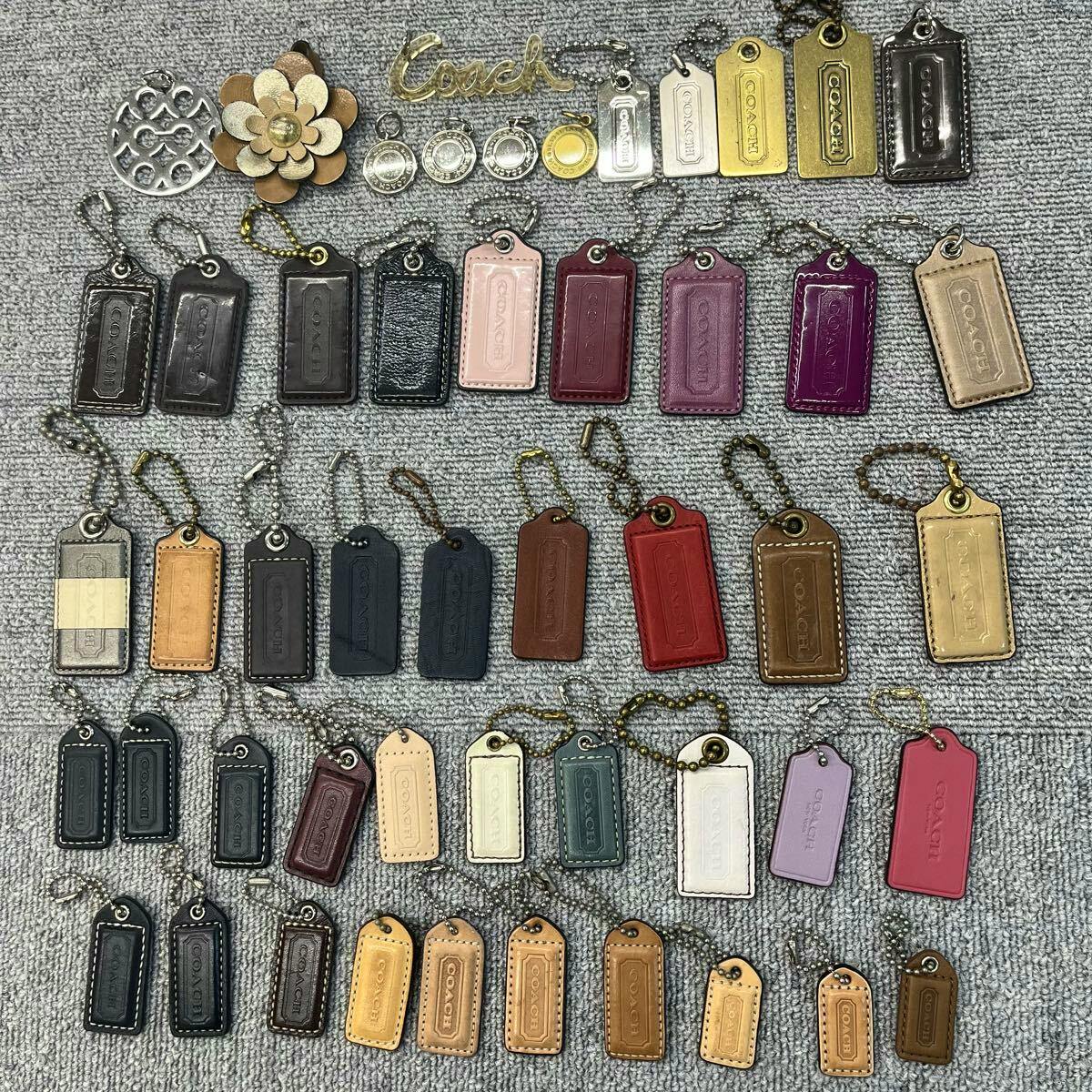 Assortment of COACH bag charms and keychain tags arranged on a gray fabric surface.