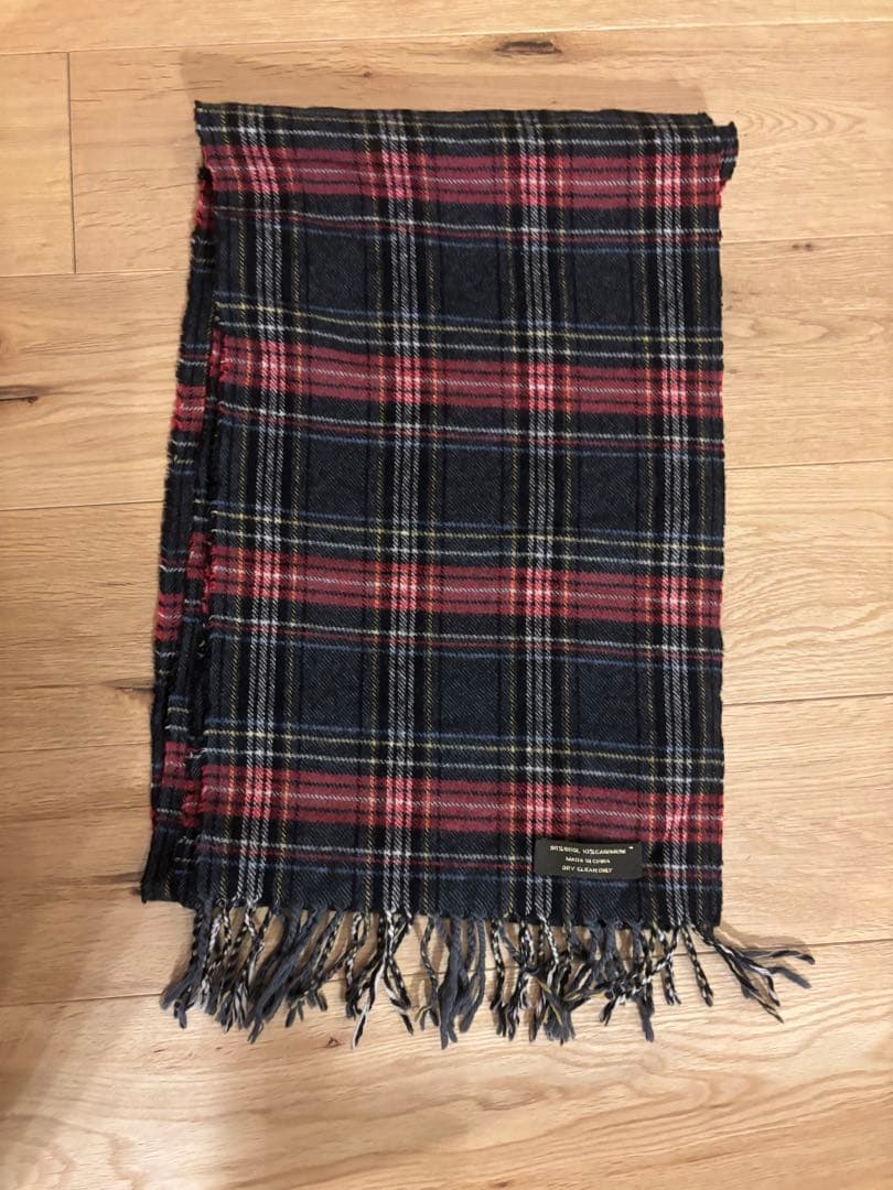 Coach plaid scarf with red and navy check pattern and fringed ends laid flat on a wooden floor.
