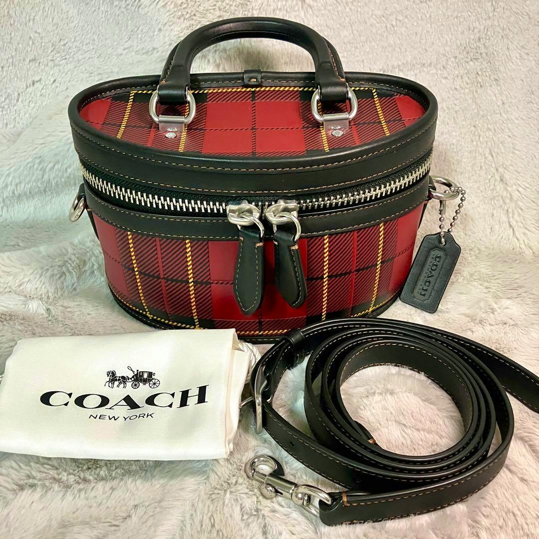 Red plaid Coach mini trail bag with black leather trim, coiled shoulder strap beside it and a Coach dust bag.