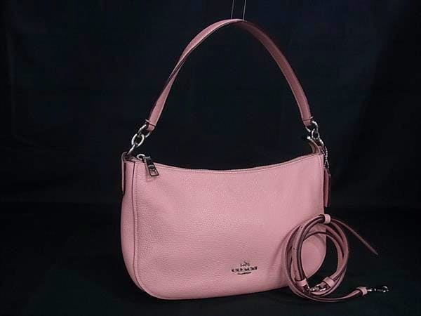 Pink Coach leather 2-way crossbody/shoulder handbag with a top handle and a coiled shoulder strap on a black background.