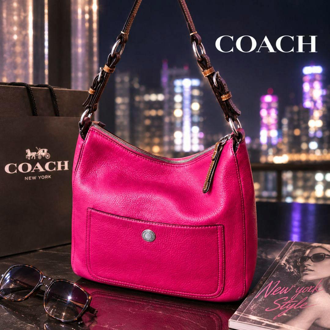 Bright pink COACH Chelsea hobo one-shoulder leather bag displayed on a table with a COACH shopping bag and sunglasses in a city-night setting.