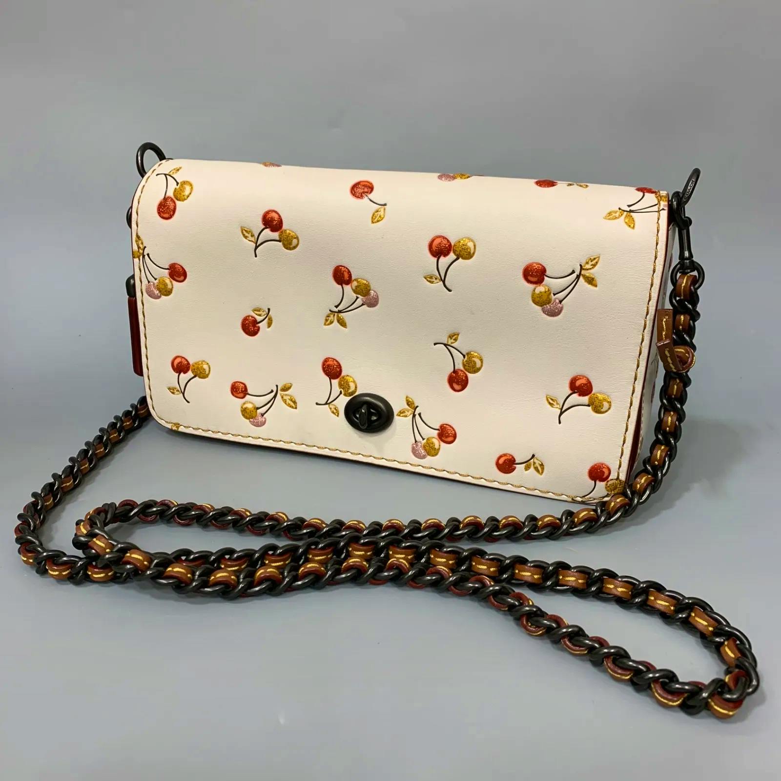 White Coach shoulder bag with cherry print, turn-lock closure, and chain shoulder strap.