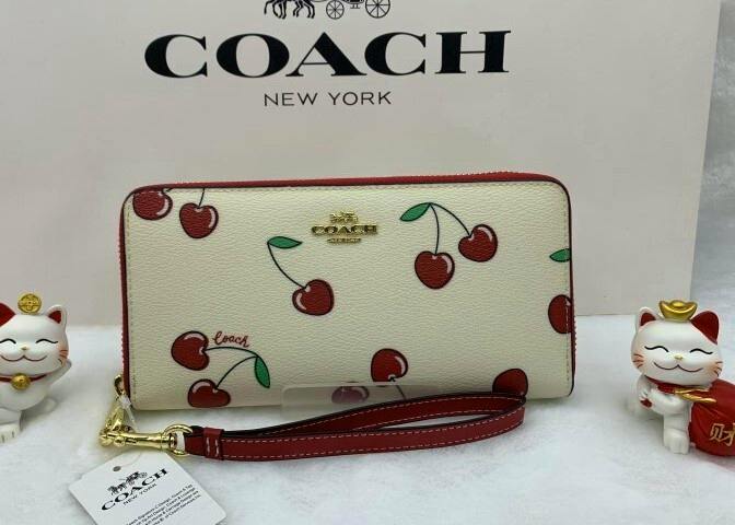 Coach long cow leather zip-around wallet with red cherry print and matching red wrist strap on a white backdrop.
