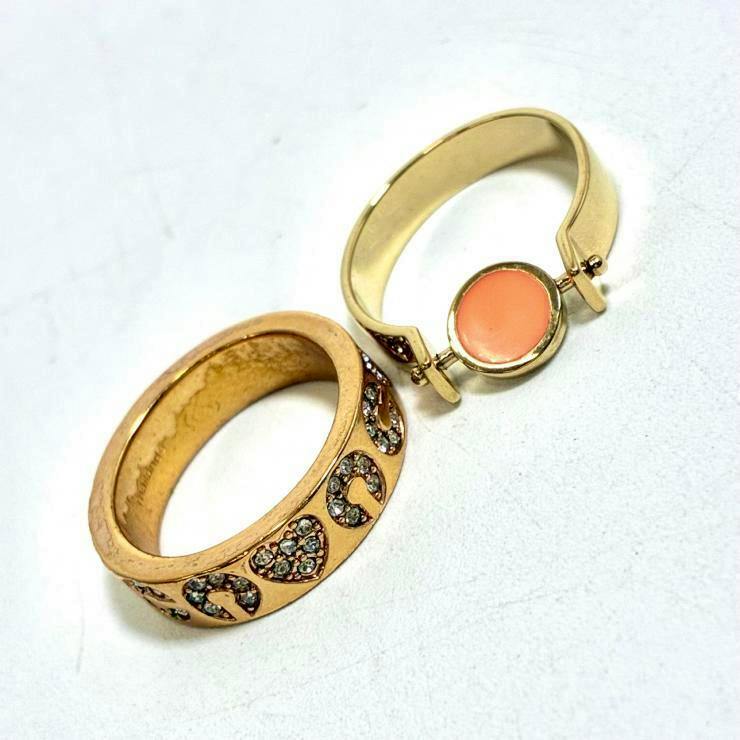 Two gold-colored rings on a white background: a wide band with rhinestone crescent/heart motifs and a narrower ring with a round pink enamel center.