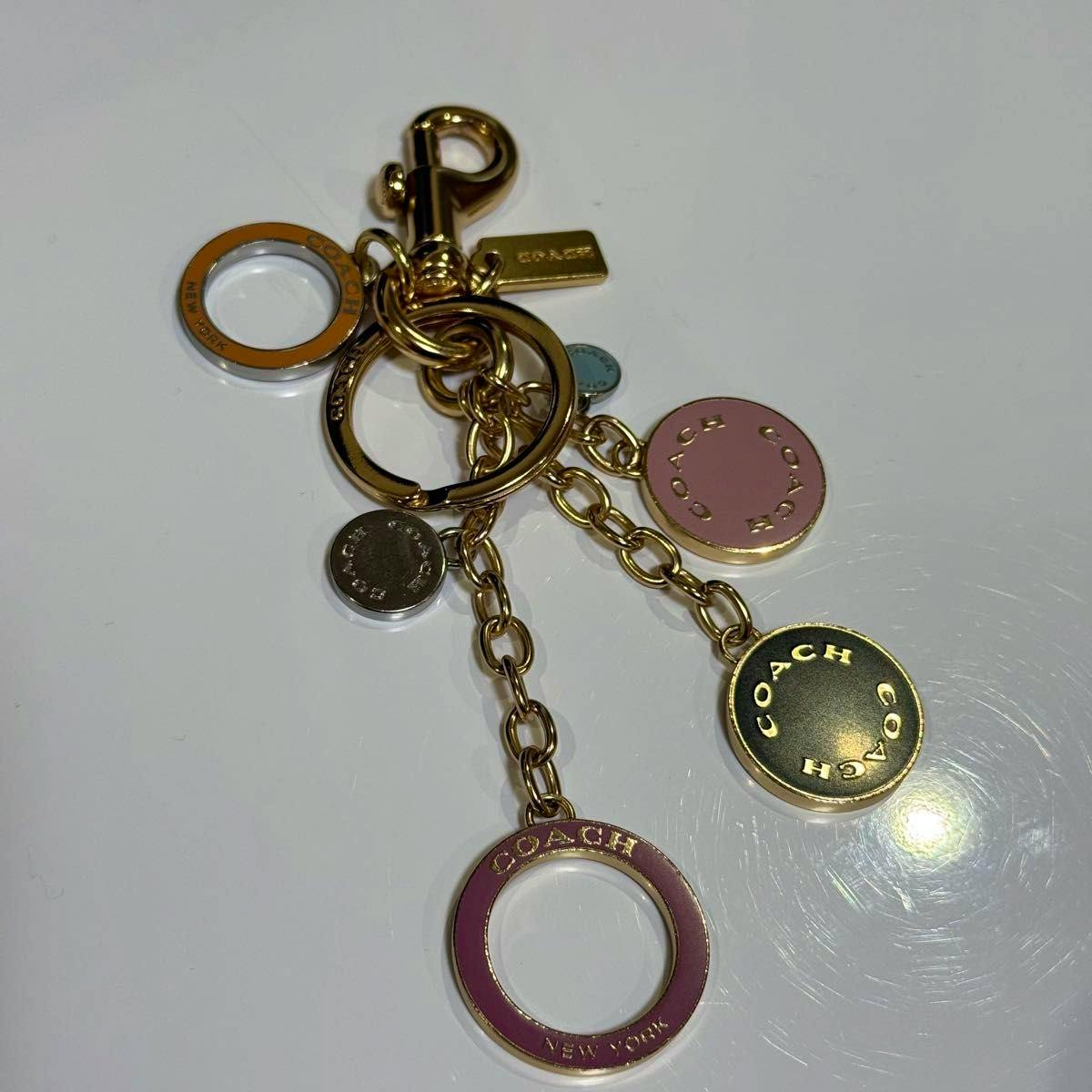 Gold-tone Coach circle cluster bag charm with multiple round disc and ring pendants laid on a white surface.