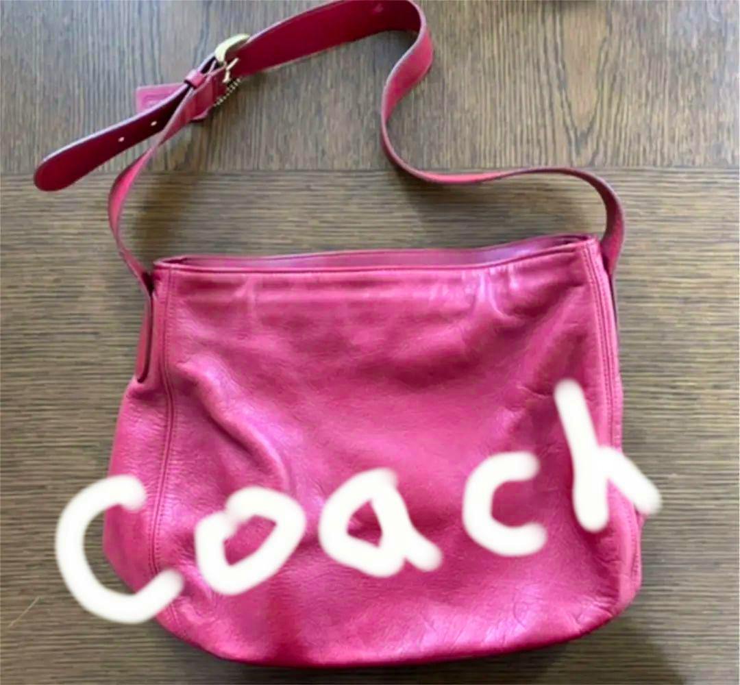 Red leather Coach handbag laid flat on a wooden surface with its shoulder strap visible.