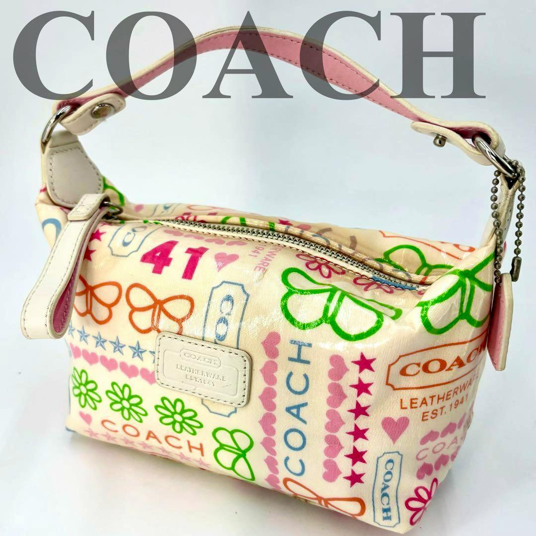 Coated-canvas pink COACH accessory pouch with colorful printed motifs and a short top handle on a white background.