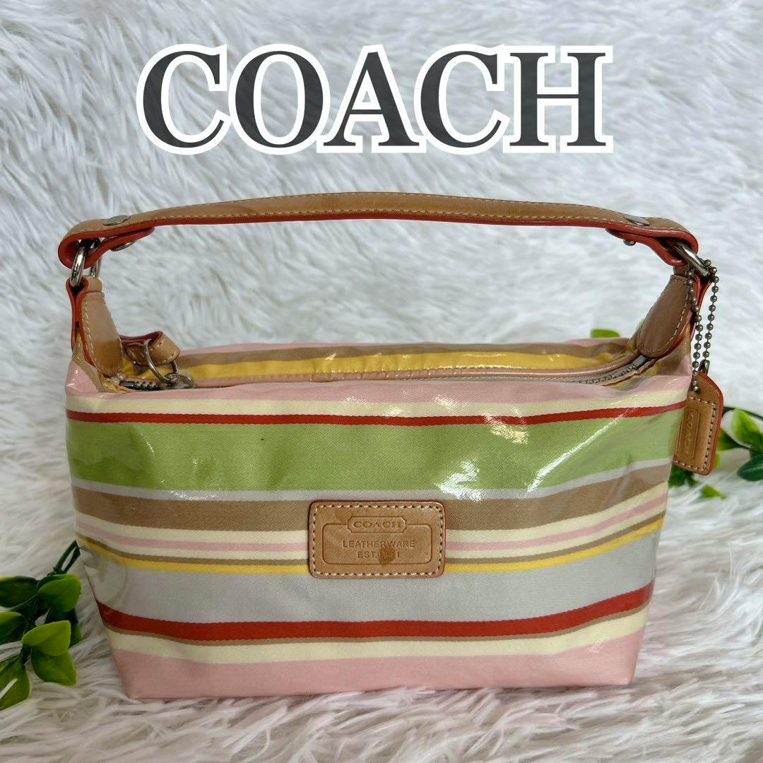 Front view of a Coach canvas accessory pouch with pink and multicolored horizontal stripes, a leather handle, and a front leather logo patch.