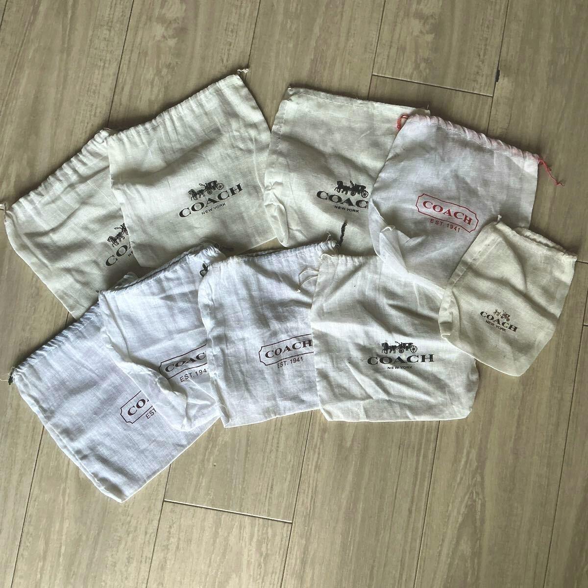 Nine white COACH drawstring cotton storage bags of various sizes with visible logos, laid flat on a wood floor showing stains and wear.