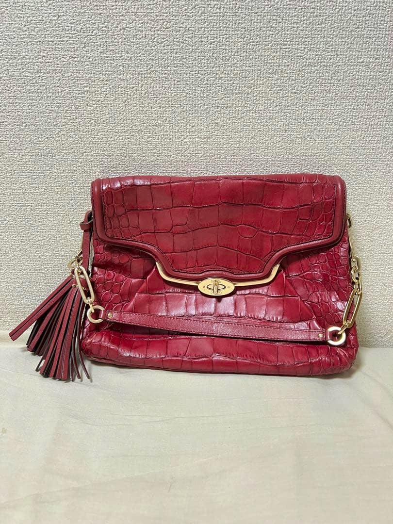 Front view of a red crocodile-embossed cow leather Coach bag with gold hardware and a tassel.