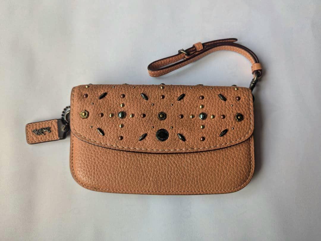 Front view of a tan Coach cow leather long wallet with wristlet strap and decorative studs on the flap.