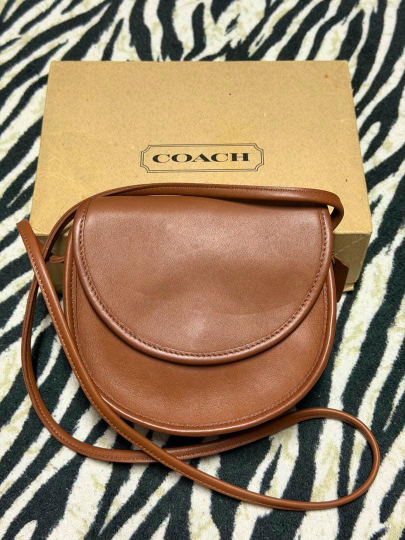 Brown Coach leather shoulder bag displayed atop a Coach box.