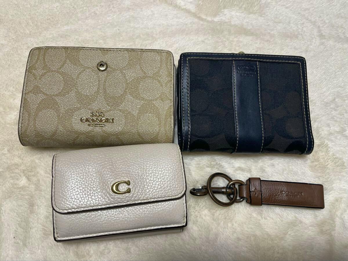 Three COACH wallets and a leather COACH key tag arranged on a light fur-like surface.