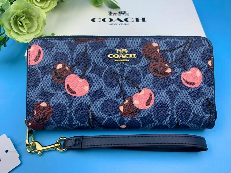 Front view of a COACH long wallet in denim signature print with pink and brown cherry motifs and a detachable wrist strap.