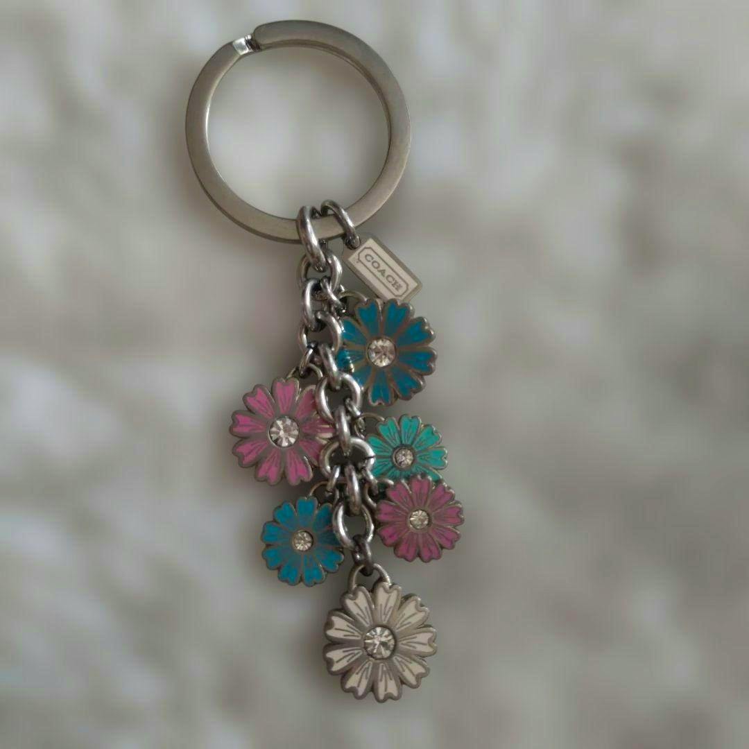 Front view of a COACH daisy-motif bag charm keyring with multiple colorful daisy charms on a metal ring.