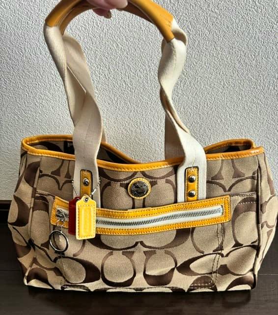 Beige Coach canvas shoulder handbag with signature C pattern, yellow trim, front zip pocket, and two short handles.