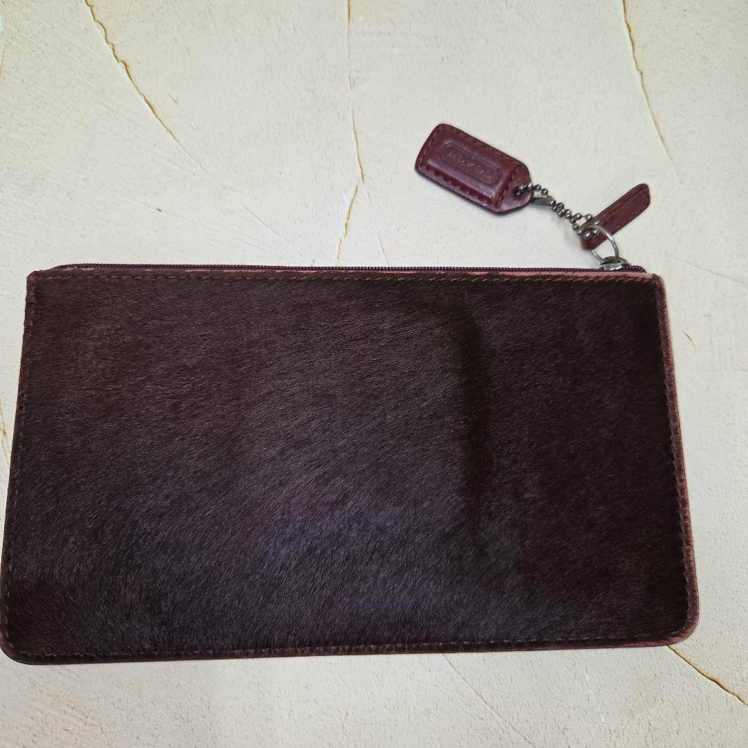 A dark brown Coach leather pouch laid flat on a light surface with the zipper and leather tag visible.