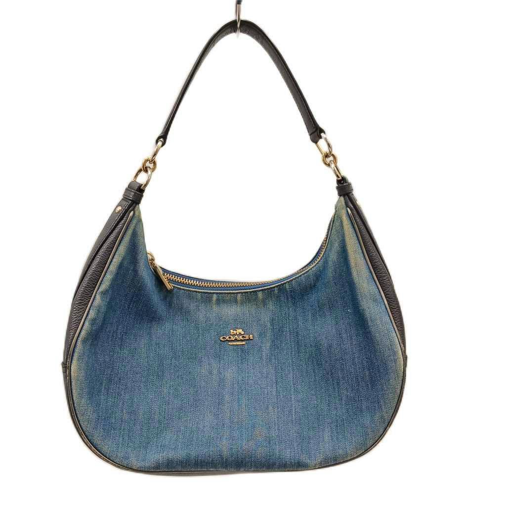 Front view of a COACH blue denim one-shoulder handbag with black leather trim, gold-tone zipper, and logo.