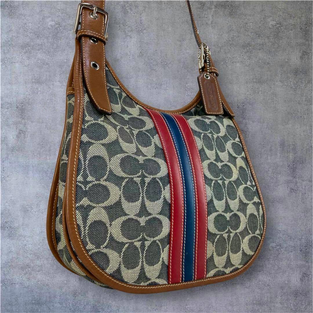 Front view of the COACH denim shoulder bag showing signature C pattern, brown leather trim, and a red and blue center stripe.