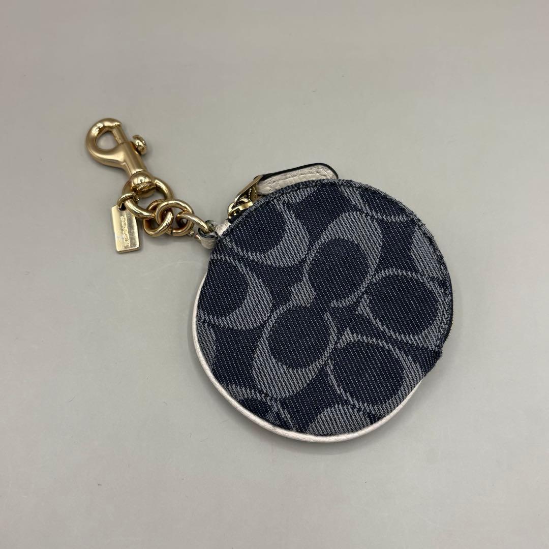 Round Coach Denim Signature coin case charm with a zinc-alloy clasp and chain on a neutral background.