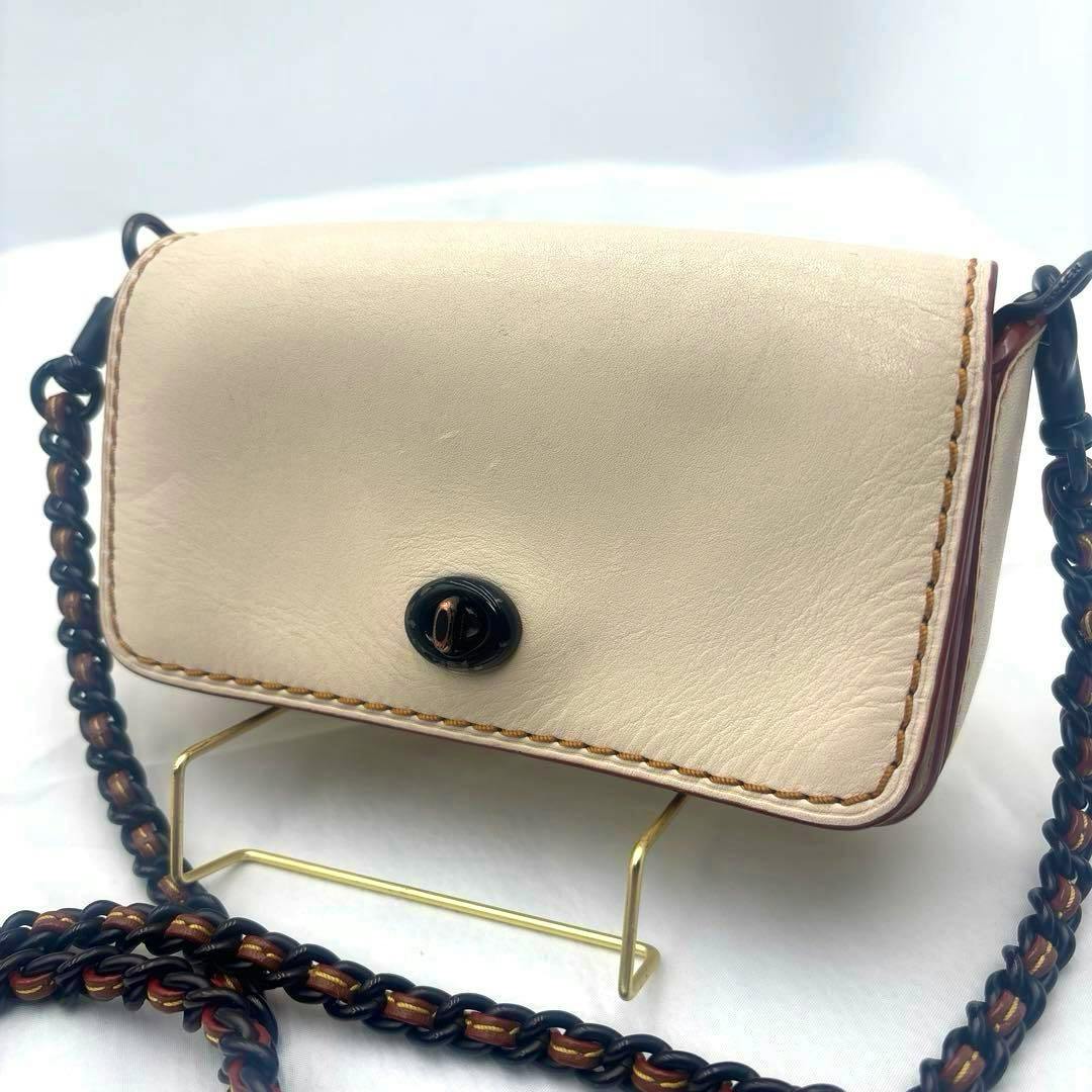 Front view of the Coach Dinky Arch chain mini pochette in light leather showing the flap with turnlock and braided chain strap.