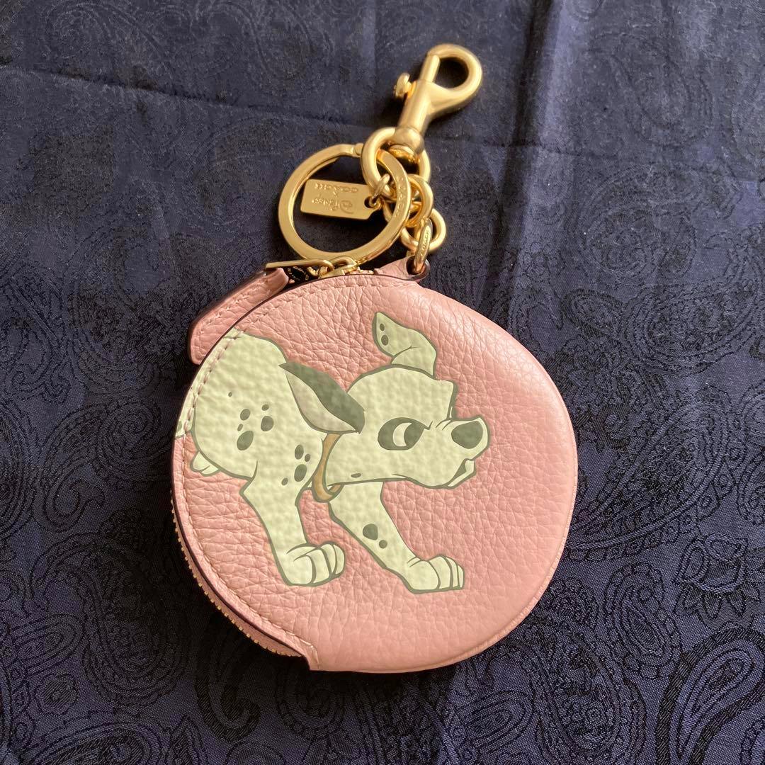 Pink round coin purse bag charm with a Disney Dalmatian print and gold keyring hardware on a dark patterned fabric.