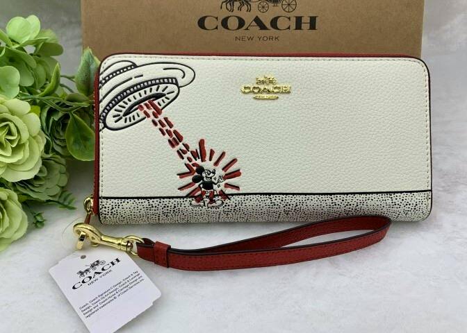Front view of the COACH synthetic leather long zip wallet featuring Mickey Mouse artwork, a red wrist strap, and attached tag.