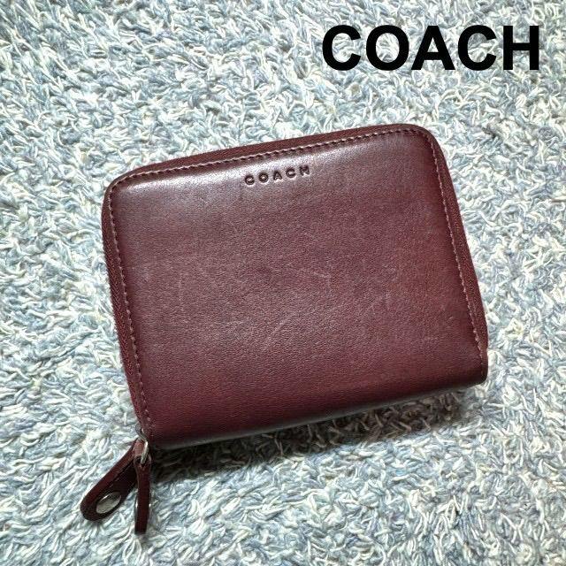 Burgundy COACH leather zip-around bifold wallet shown on a textured surface with visible zipper pull.