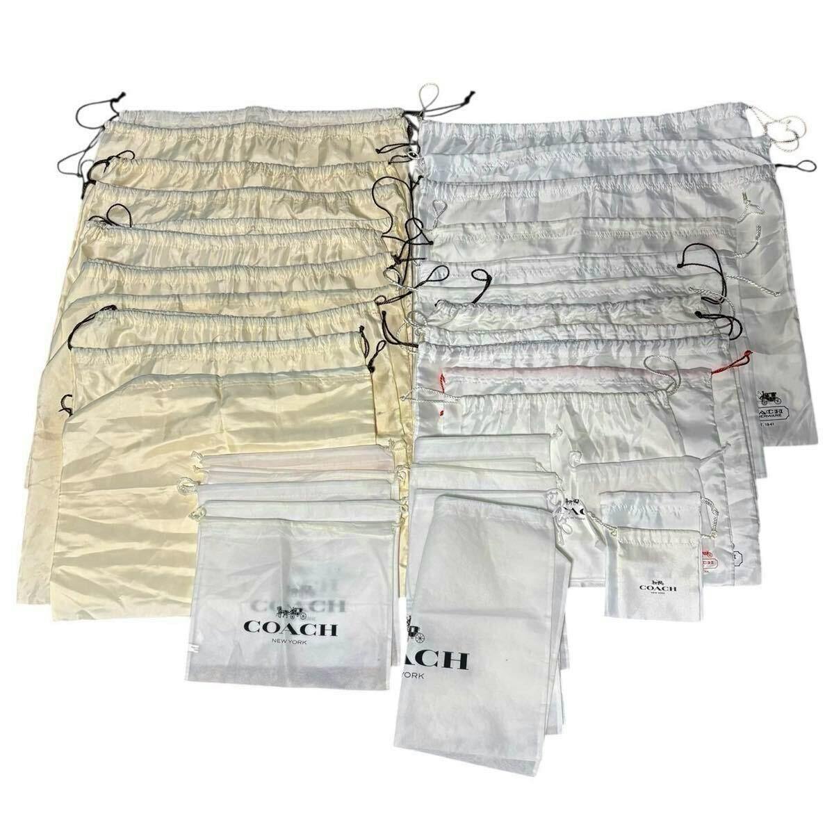 Many white and cream COACH drawstring dust bags and pouches arranged flat, several showing the COACH logo.