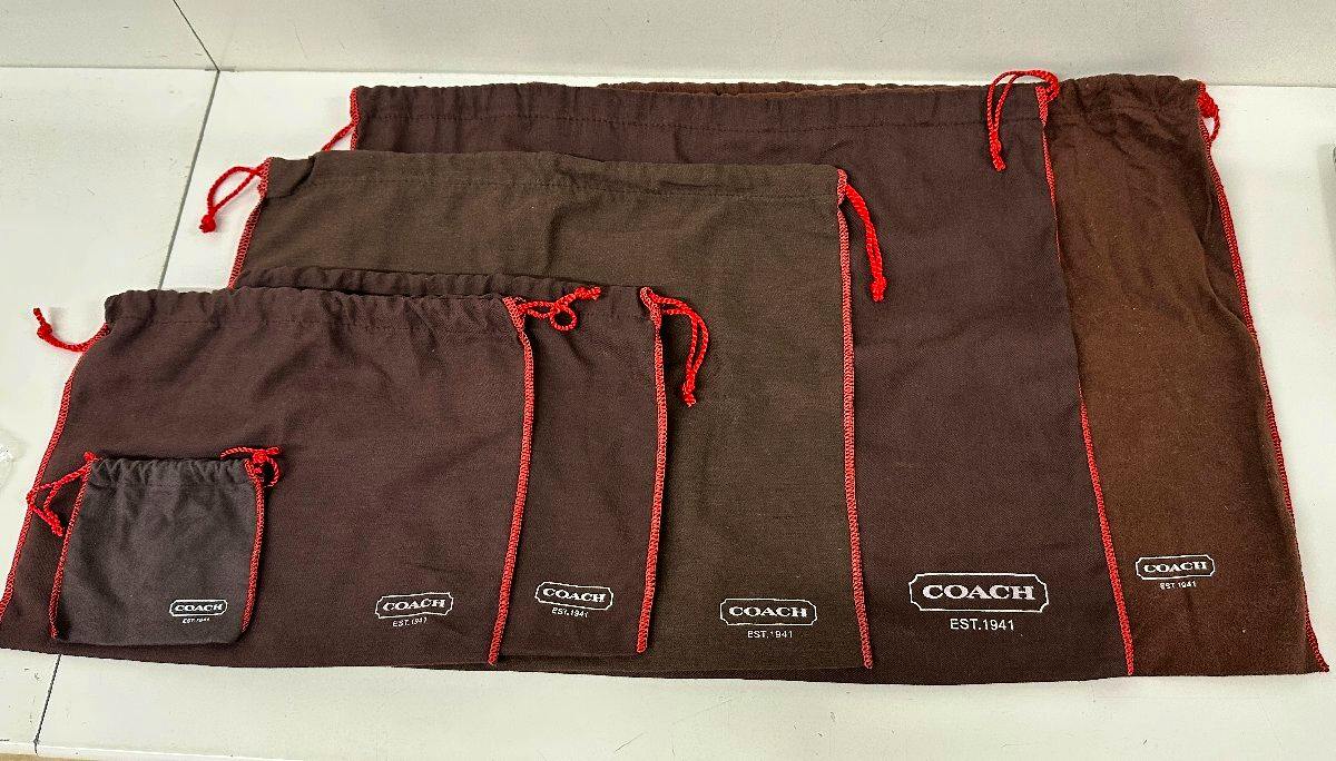 Multiple brown COACH cloth dust/storage bags in different sizes with red drawstrings and COACH logos laid flat on a surface.
