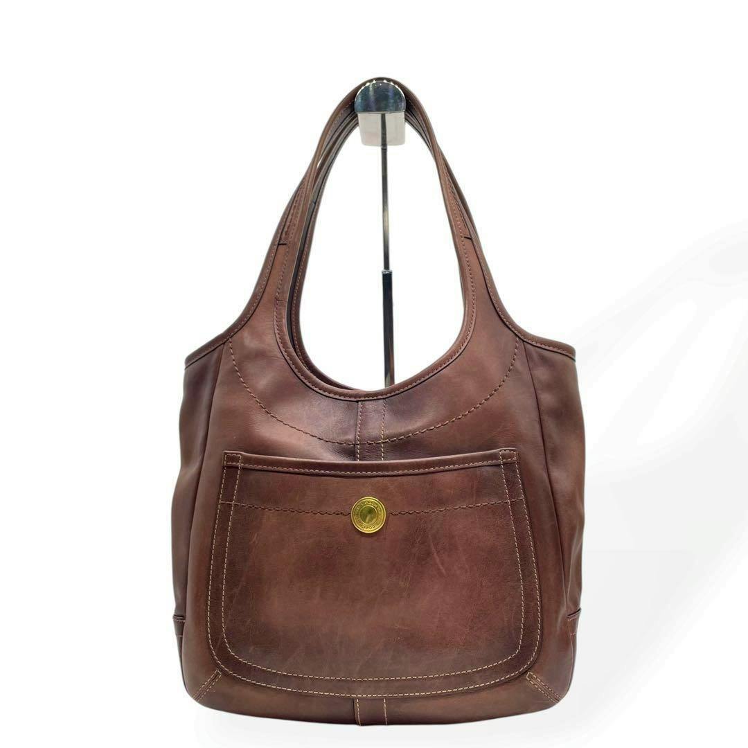 Front view of a brown leather COACH tote bag with a front pocket and gold-tone round hardware.