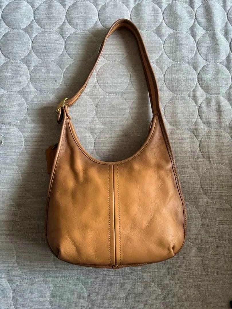 Brown Coach cow leather shoulder bag laid flat showing the front and strap on a quilted surface.
