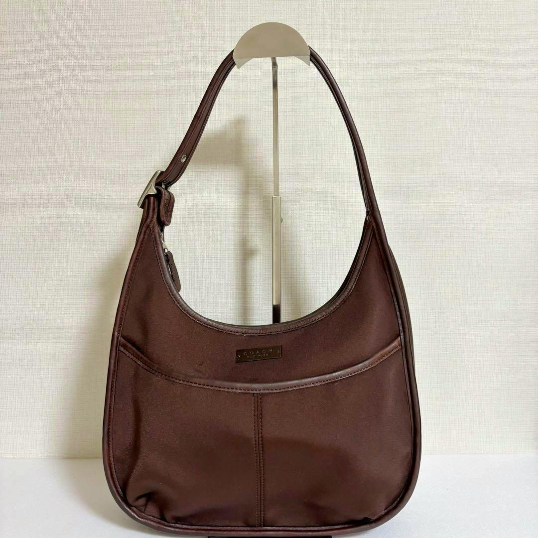 Brown COACH Ergo Style leather shoulder bag hanging on a stand against a light wall.