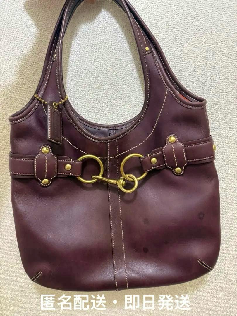 Front view of a burgundy Coach leather Ergo tote bag showing brass horsebit hardware and some scuff or stain marks on the leather.
