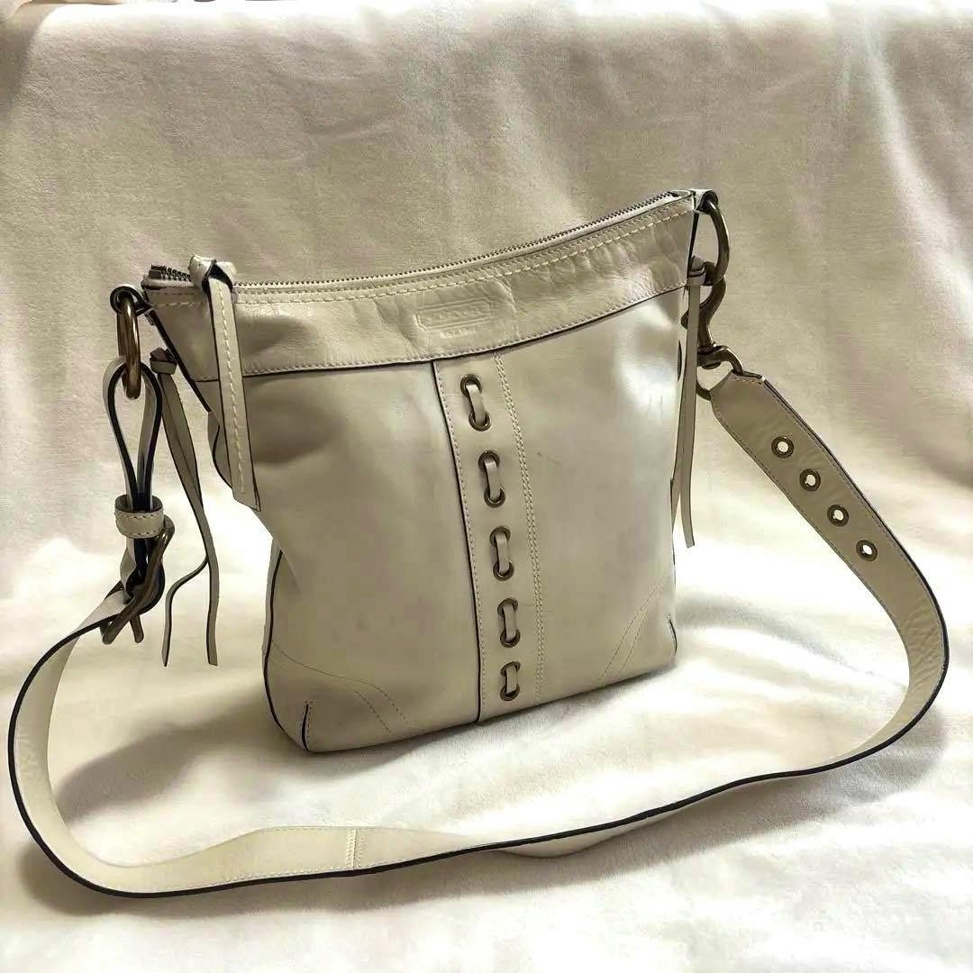 Light-colored COACH eyelet shoulder bag in synthetic leather shown front view with long adjustable strap and eyelet detailing.