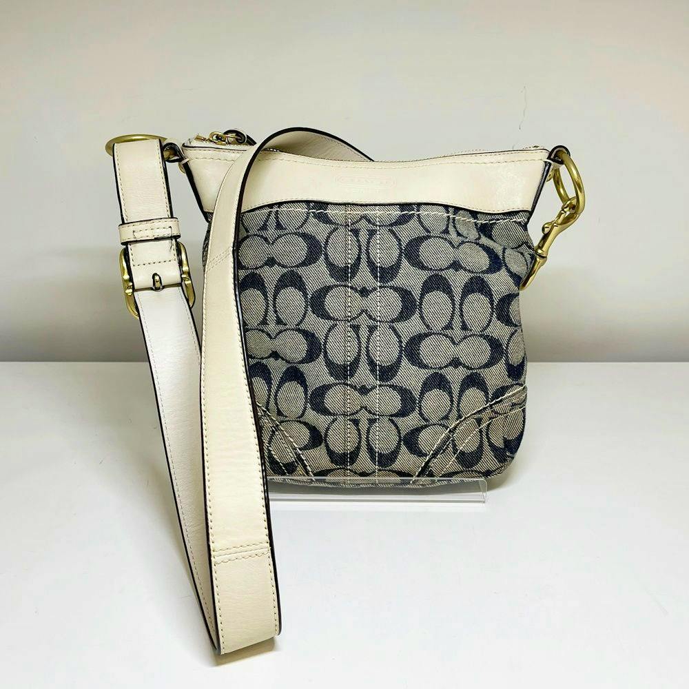 Front view of a COACH signature canvas shoulder bag with cream leather trim and an adjustable strap.