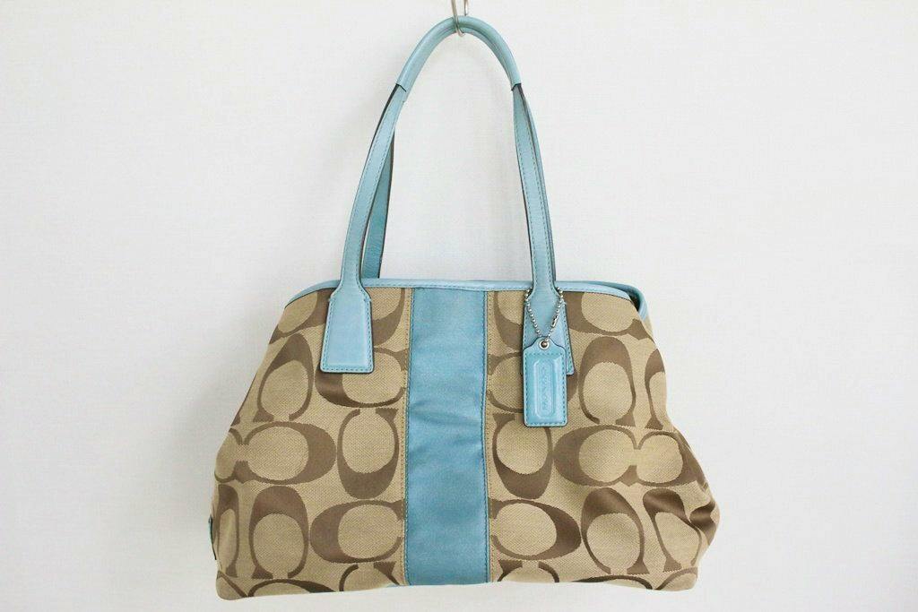 Front view of a beige Coach canvas handbag with signature 'C' pattern and light blue leather trim and handles.