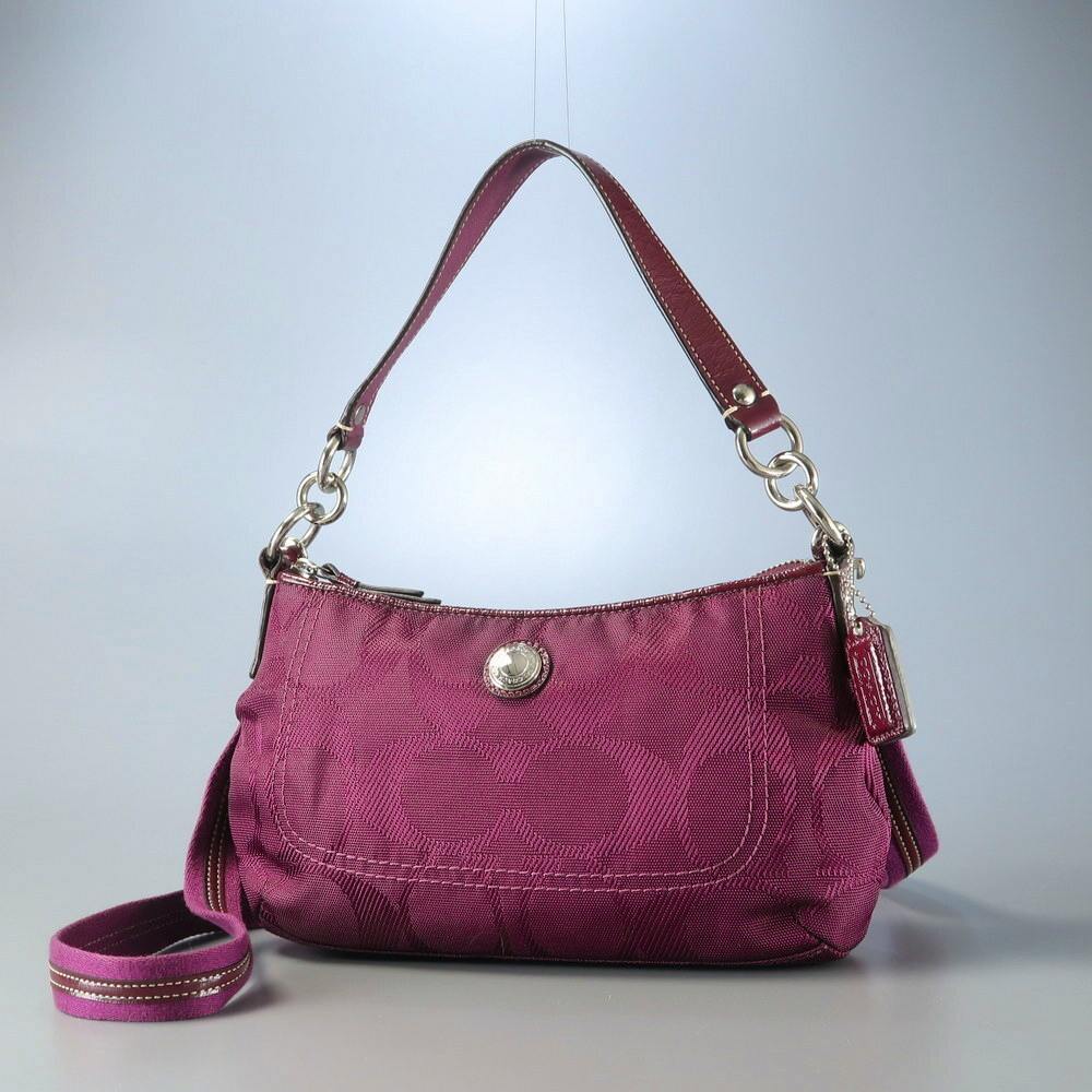 Front view of a purple Coach signature-pattern shoulder bag showing a short leather handle and a long crossbody strap.