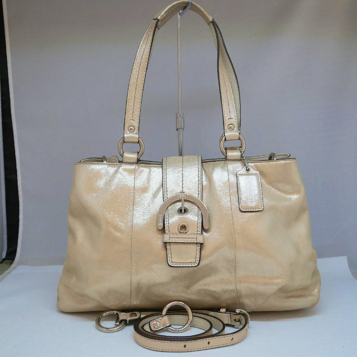 Front view of a gold-toned COACH 2way tote/shoulder bag with buckle detail and a coiled detachable strap.