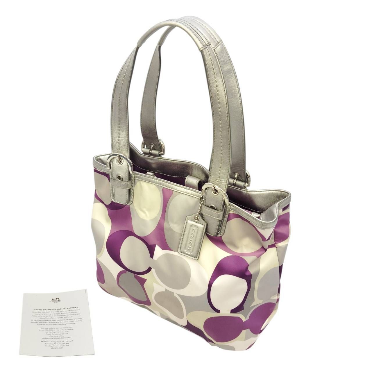 Purple and beige Coach satin op-art tote bag with silver handles and visible logo hang tag, photographed with a paper card.