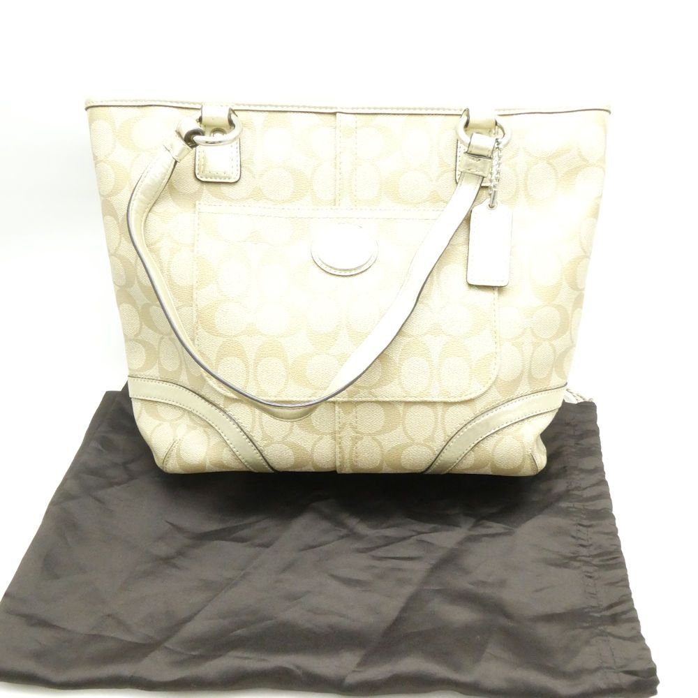 Beige Coach signature canvas tote bag with shoulder straps displayed on a dark dust bag.