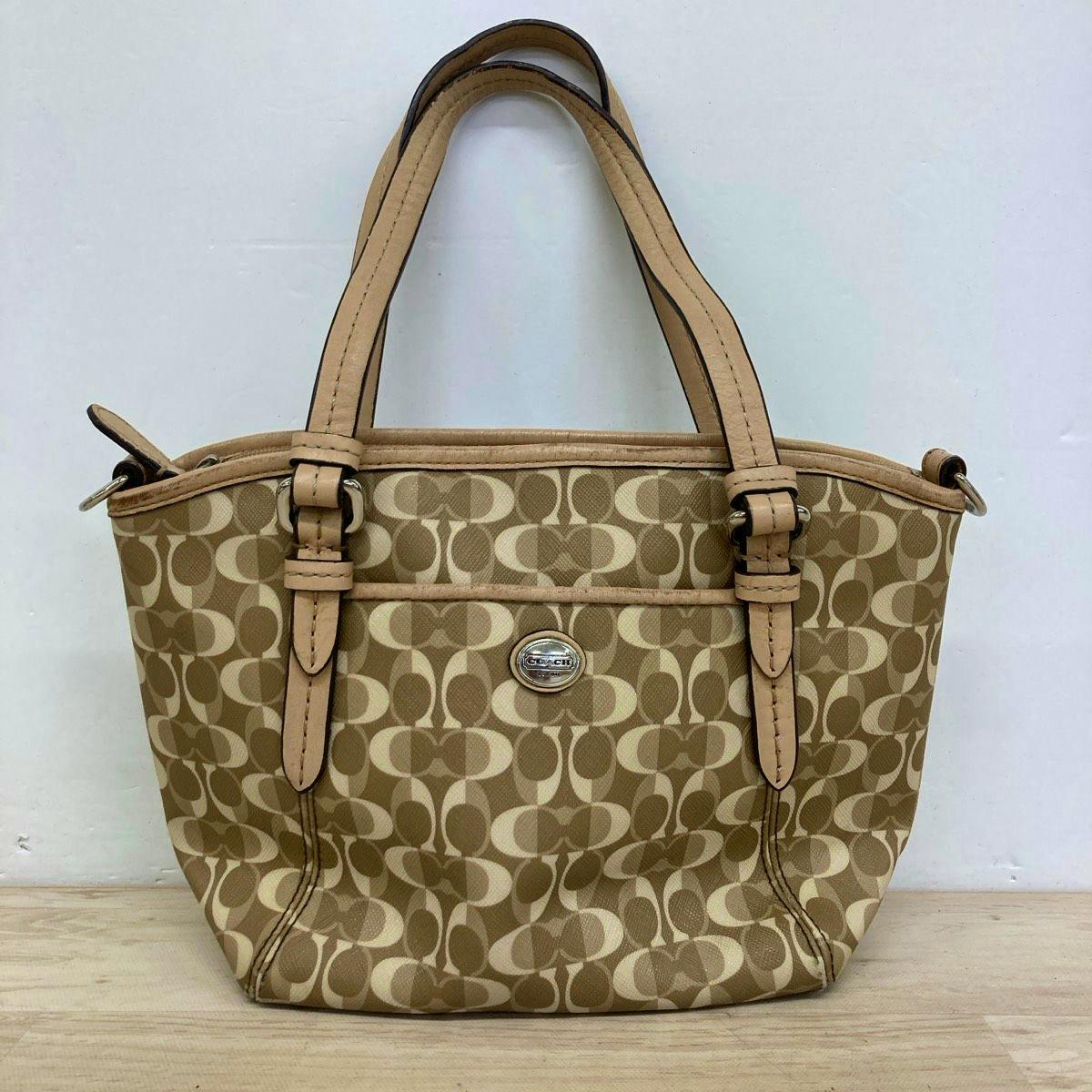 Front view of a beige Coach F26401 signature canvas tote handbag with leather straps and a logo medallion.