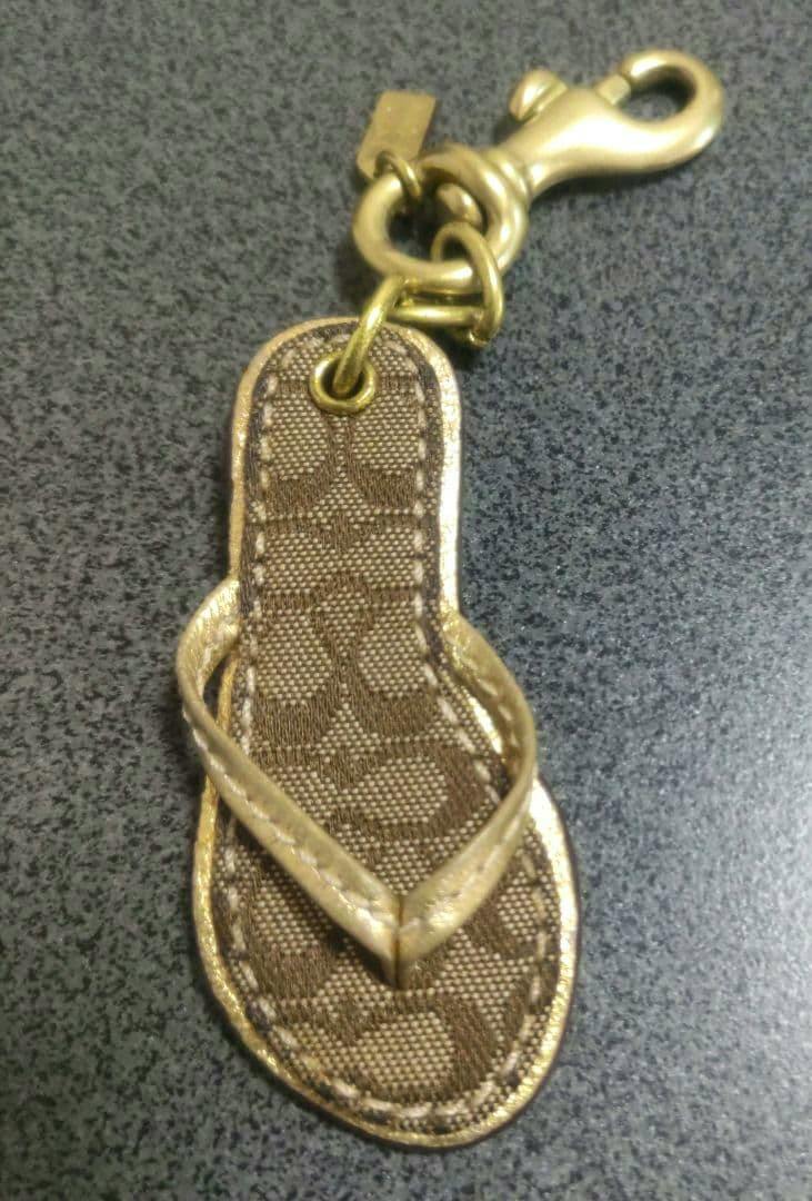 Front view of a flip‑flop shaped COACH keychain showing the monogram-patterned footbed, gold-tone V-strap and clasp.