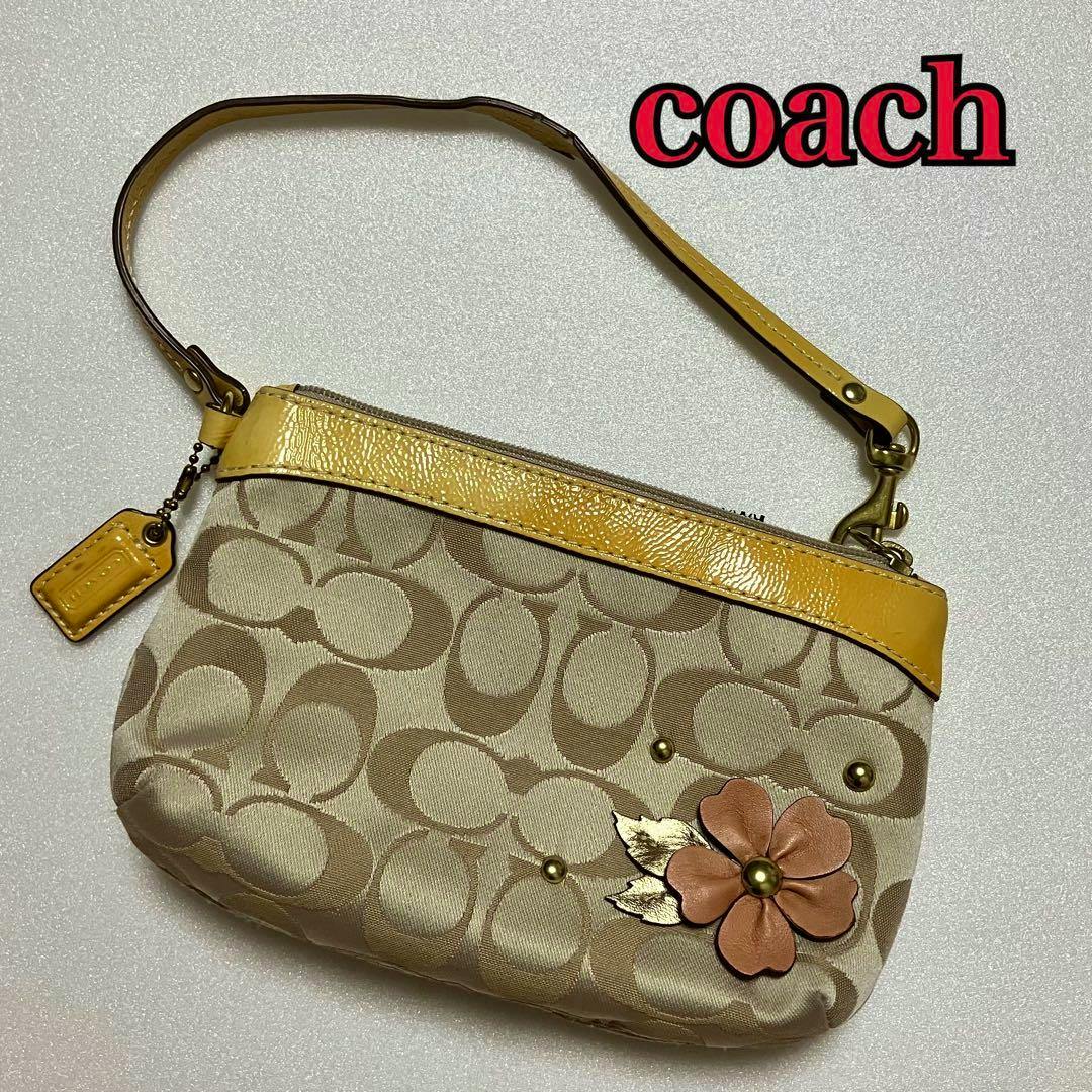 Front view of a Coach canvas hand pouch with signature C pattern, yellow trim and a flower decoration on the front.