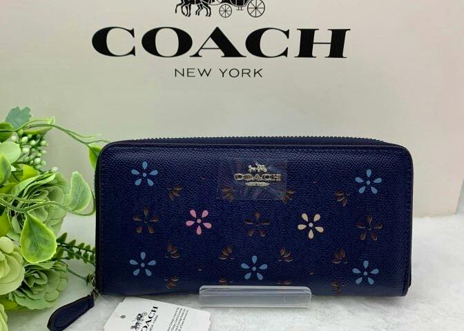Navy COACH long zip-around wallet with floral pattern and metal logo, shown in front of a COACH box.