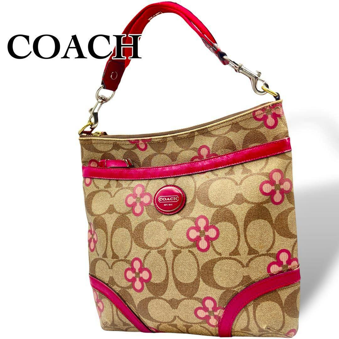 Front view of a brown Coach shoulder bag in signature canvas with pink floral accents, pink trim, and a round Coach logo plate.