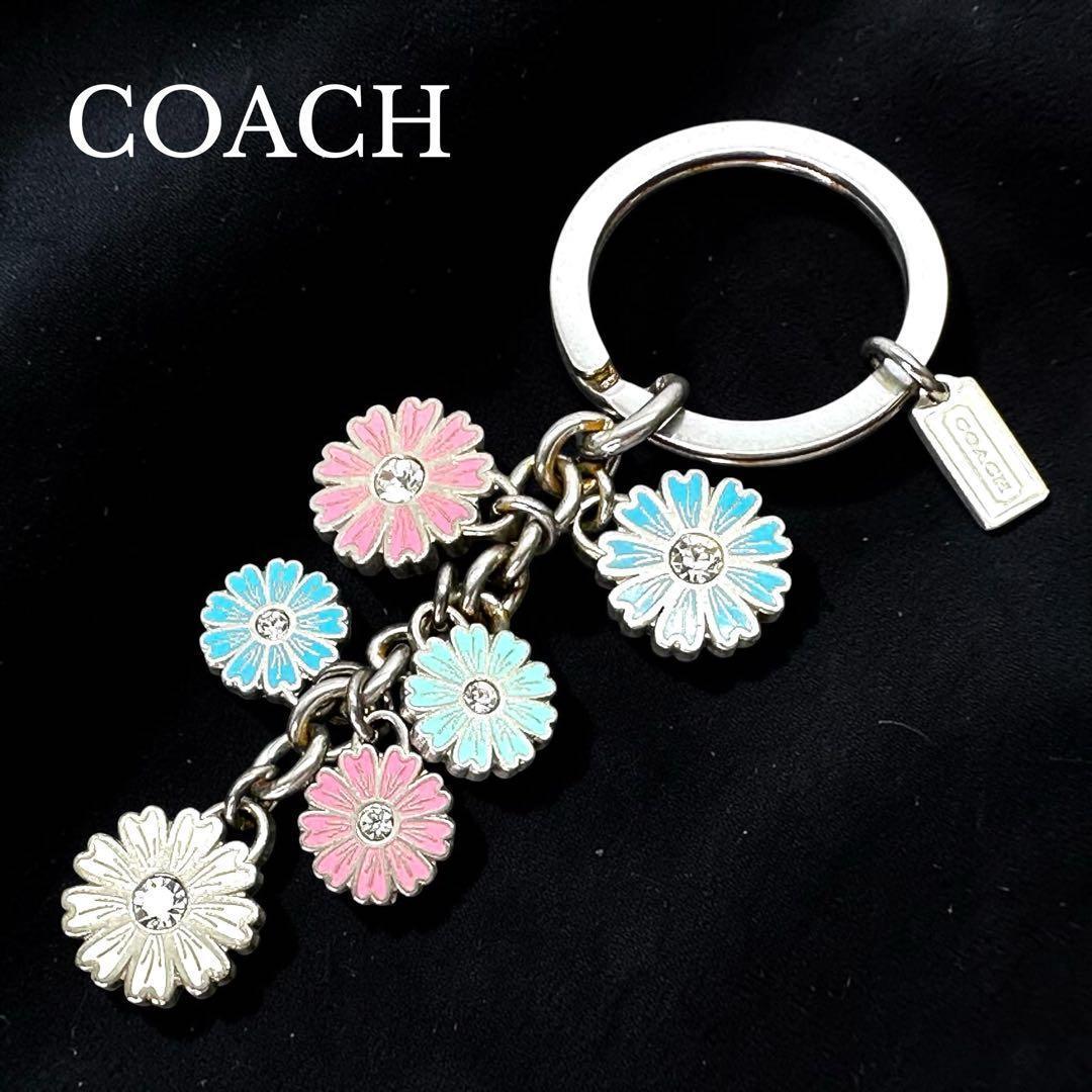 COACH flower charm keychain with multiple pastel enamel daisy charms on a metal key ring against a black background.